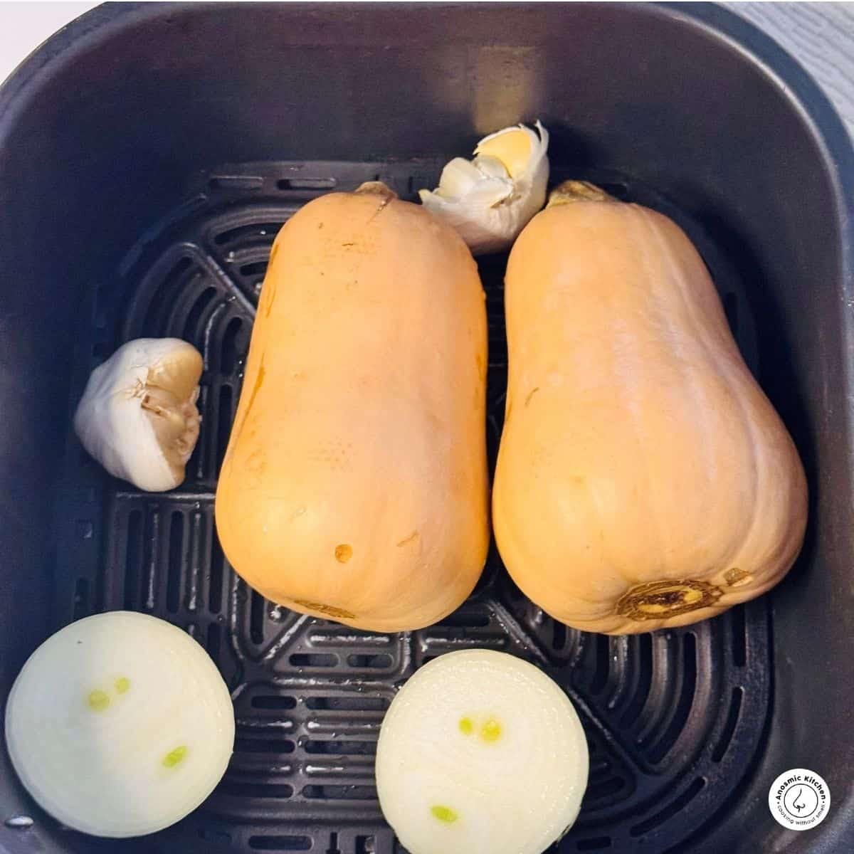 raw butternuts, halved onion and halved garlic bulb in air fryer basket