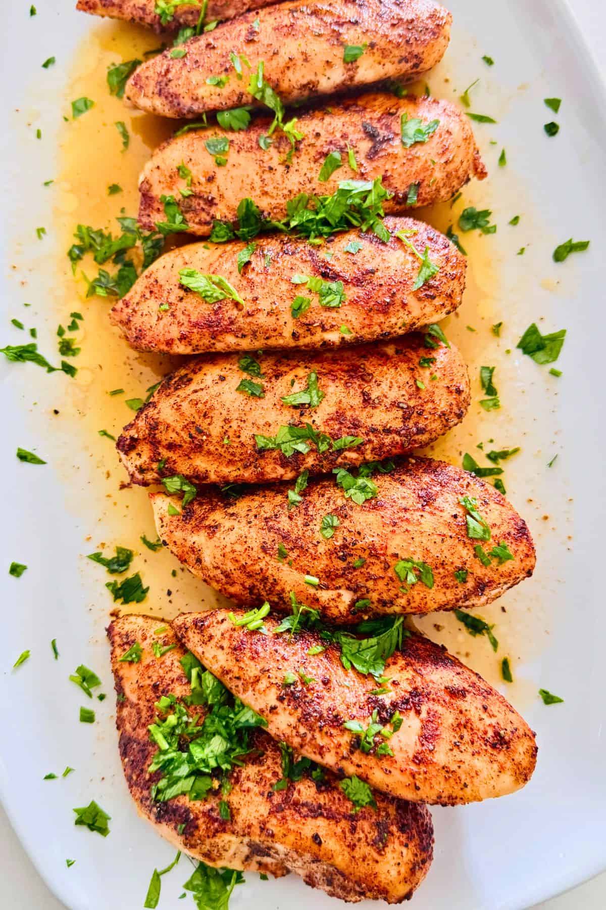 chicken breast fillets stacked on a serving platter garnished with fresh parsley