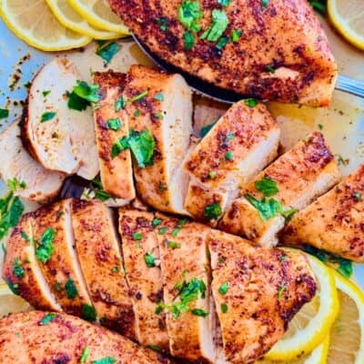 Oven-baked chicken breasts sliced and served on a platter with lemon slices