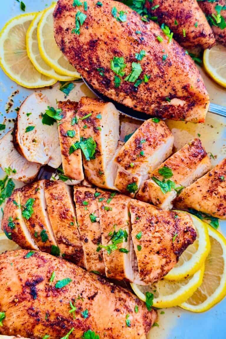 Oven-baked chicken breasts sliced and served on a platter with lemon slices
