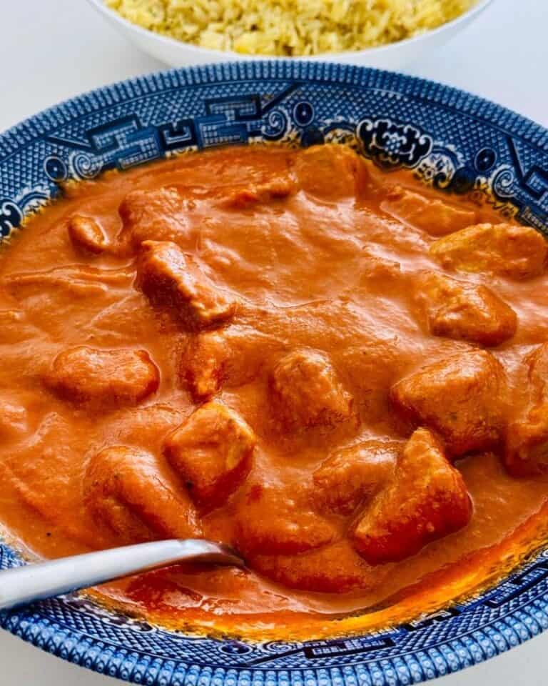Dairy-free chicken curry made with cubed chicken breast in a thick, tomato-based curry sauce, served in a blue floral bowl with a serving spoon.