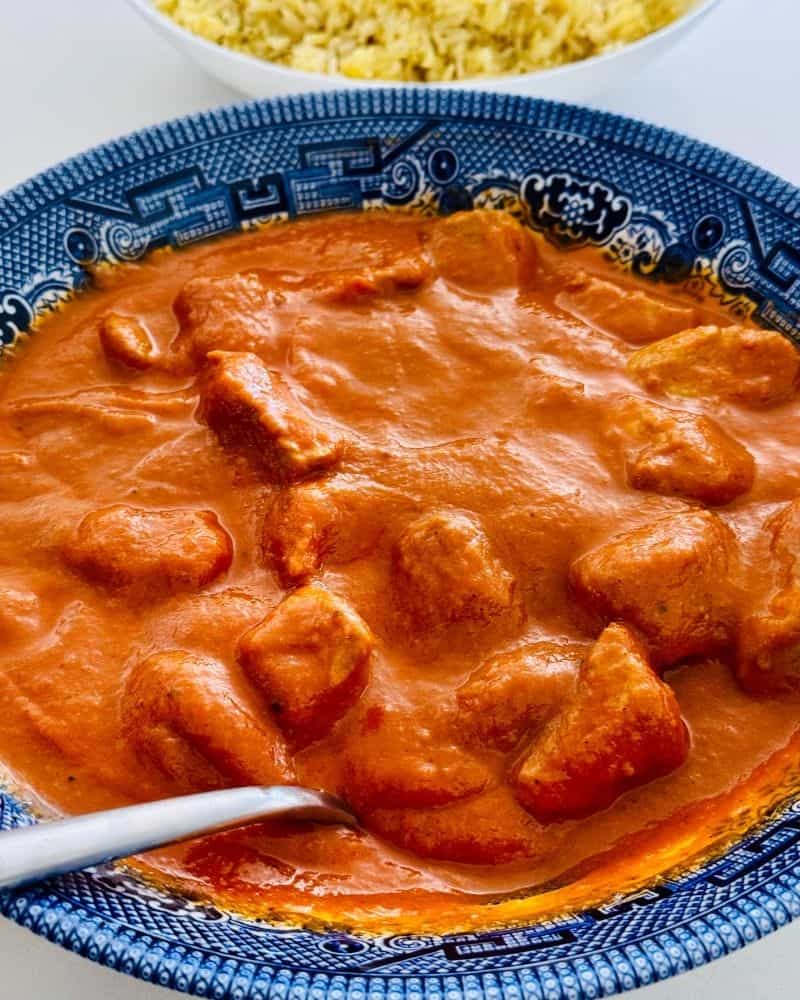 Dairy-free chicken curry made with cubed chicken breast in a thick, tomato-based curry sauce, served in a blue floral bowl with a serving spoon.