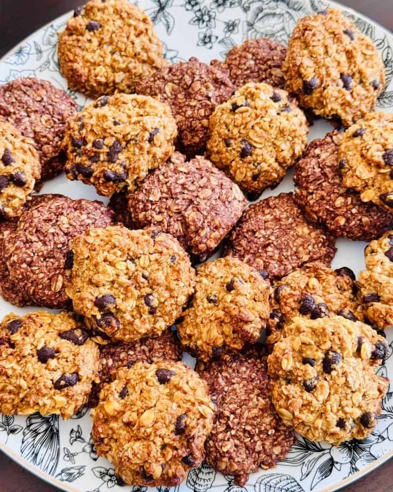 Pile of gluten-free oat flour cookies on a plate, showing a mix of soft golden cookies with chocolate chips and darker cocoa-based cookies with oats visible on the surface