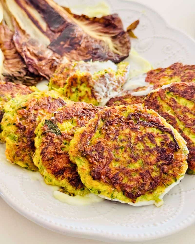 Crispy zucchini fritters served on a white plate, partially overlapping with roasted radicchio on the side