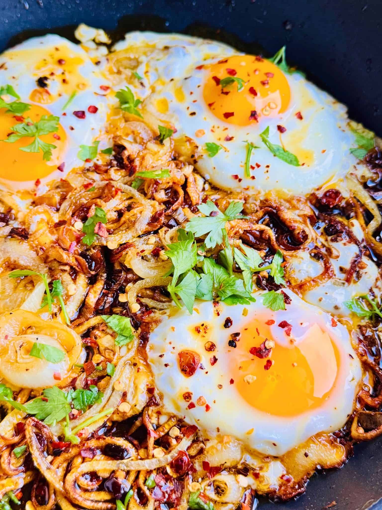 fried eggs and caramalised onion rings in oil garnished with fresh parsley