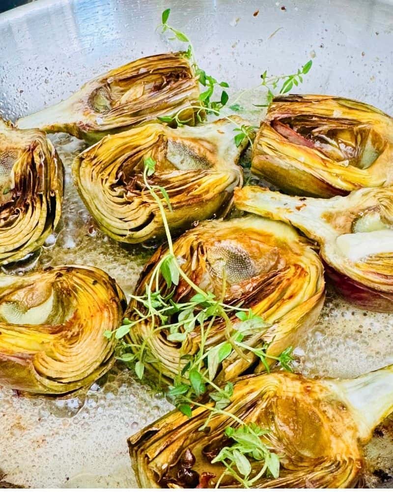 Golden brown sautéed artichokes in a skillet with fresh thyme and melted butter.