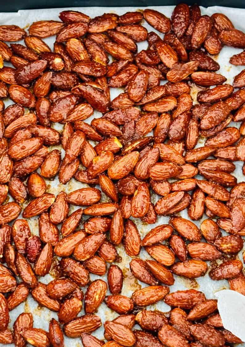 sticky sweet and spicy air fryer roasted almonds spread out to cool on parchment paper