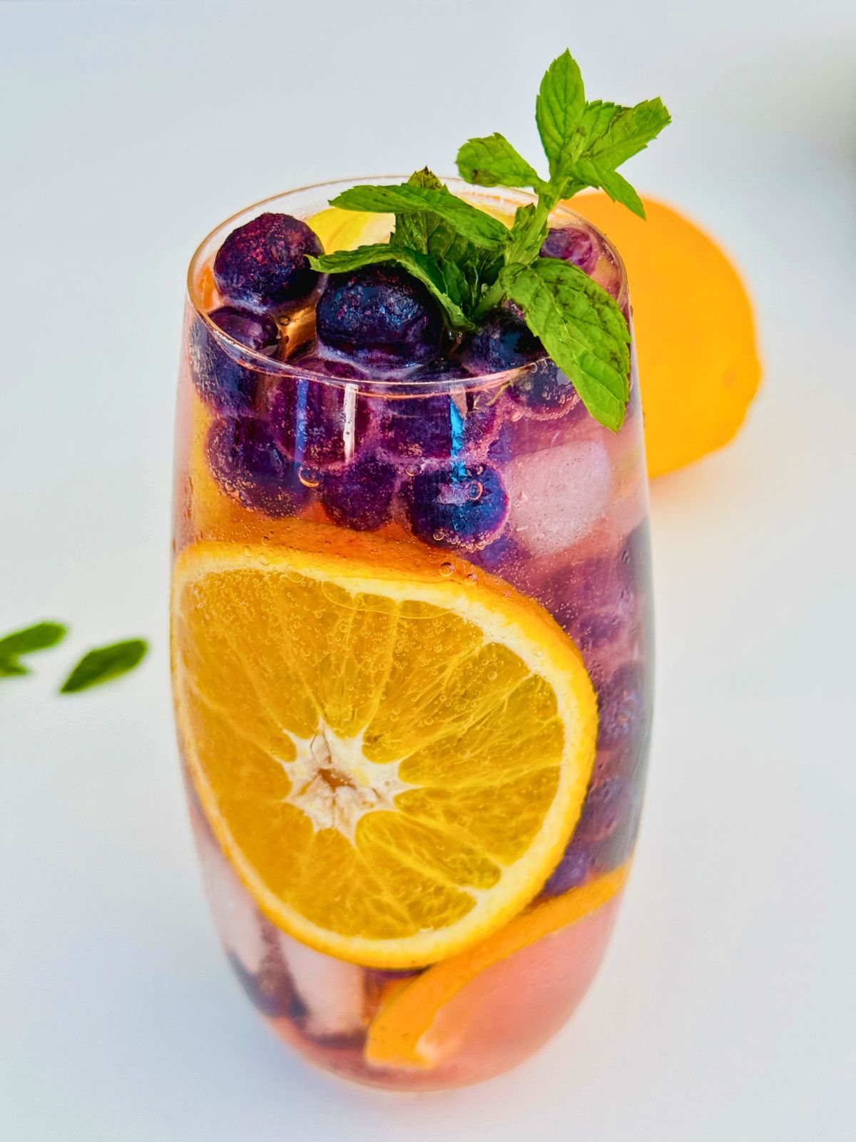 a glass with ice, blueberries, orange slices and fresh mint