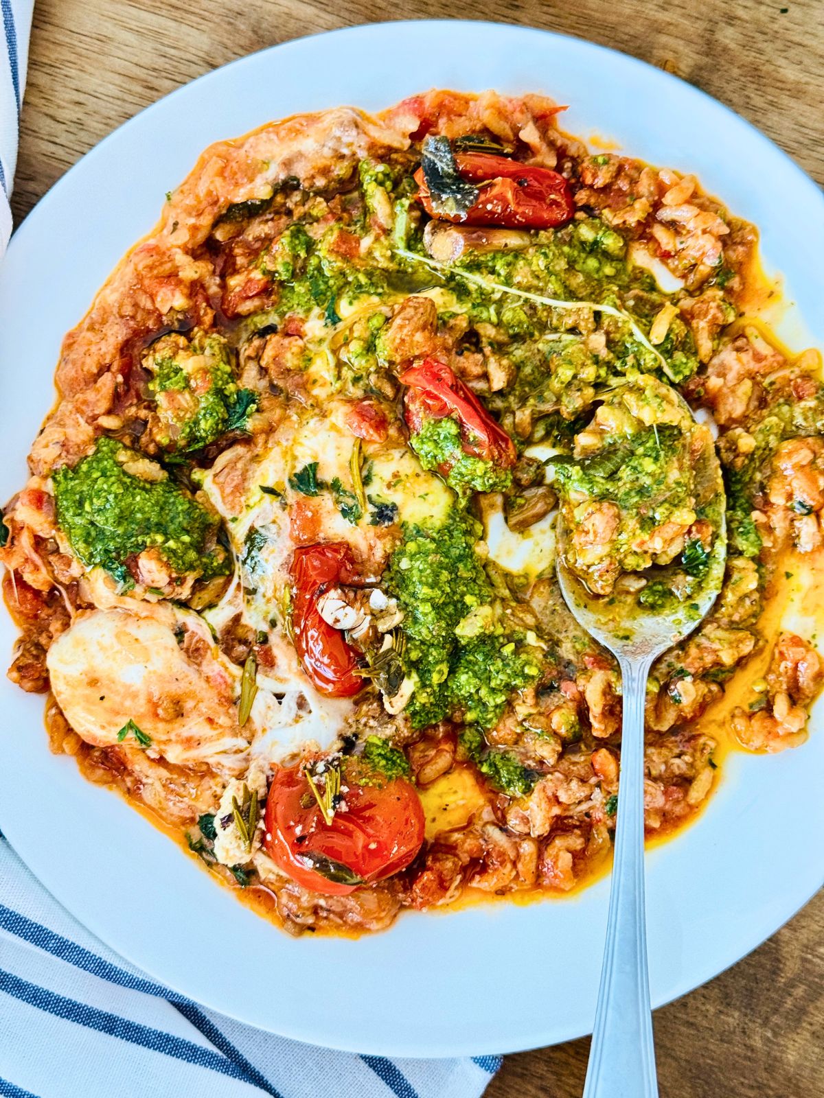 tomato risotto in a white plate with pesto over and a spoon to eat.
