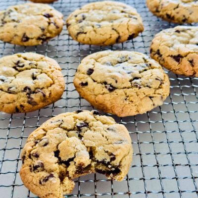 Baked chocolate chip cookies on a cooling rack, one with a bite taken out