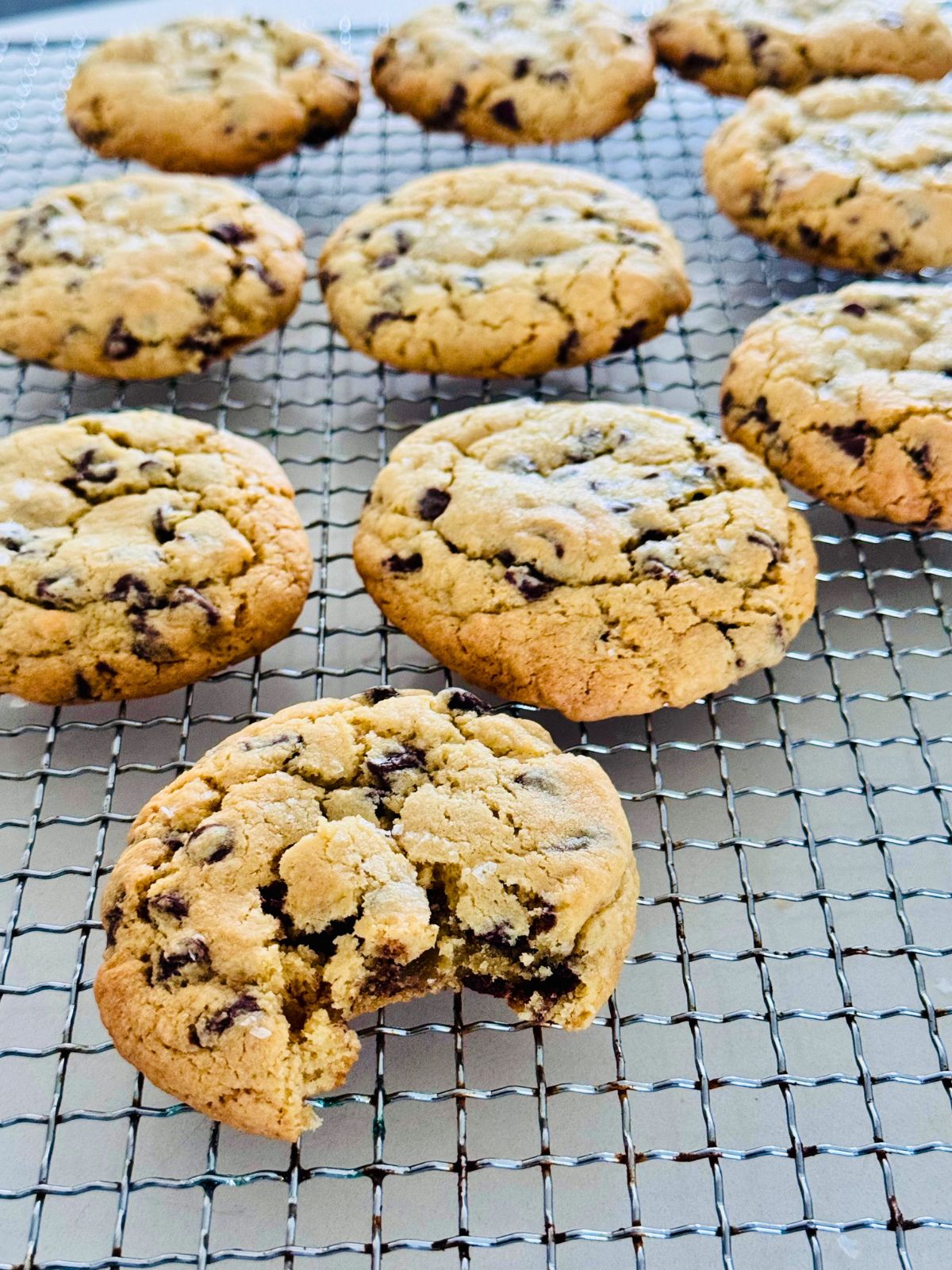 Baked chocolate chip cookies on a cooling rack, one with a bite taken out