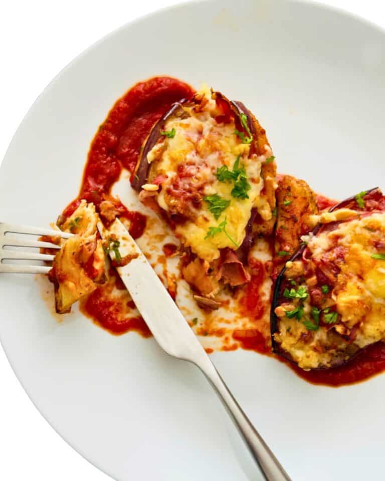 Chicken eggplant and Parma ham bake served on a white plate with tomato sauce and melted cheese