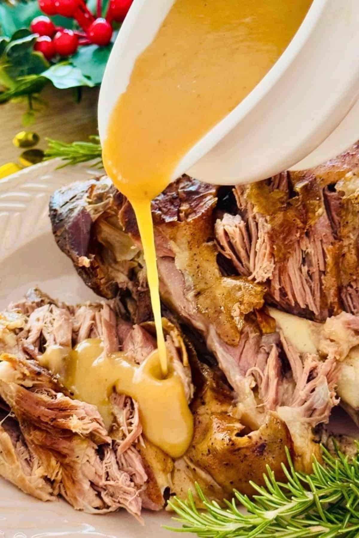 Fall-apart tender roasted lamb leg with yellow sauce being poured over, juicy and golden, ready to serve