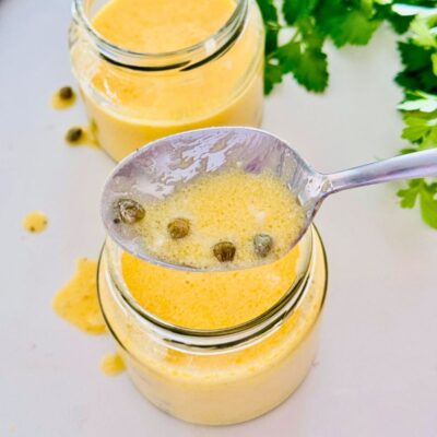 lemon butter sauce in jar showing off some of the sauce in a spoon with capers.