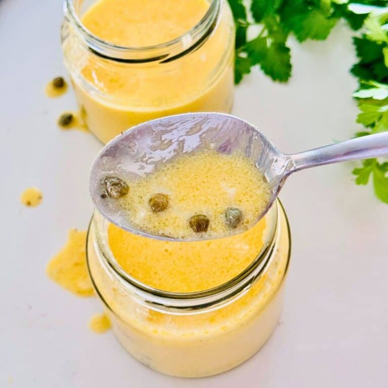 lemon butter sauce in jar showing off some of the sauce in a spoon with capers.