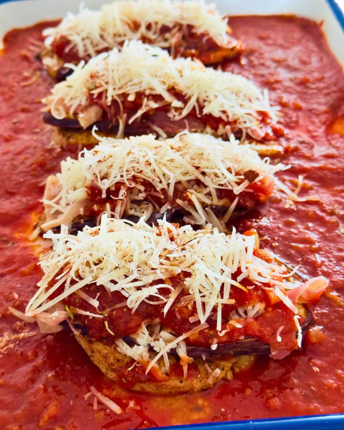 Chicken fillets topped with grilled eggplant, Parma ham, tomato sauce and cheese in a baking dish before baking