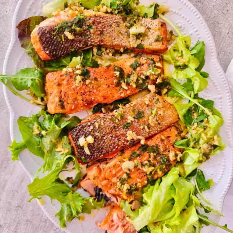 cooked salmon fillets over a bed of lettuce on a white serving platter