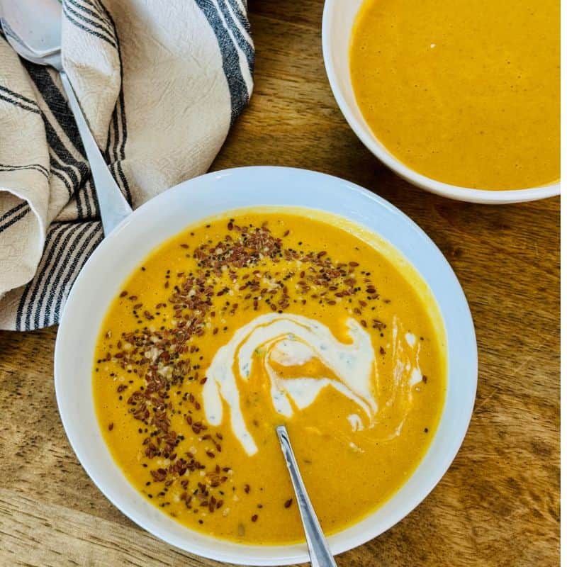 yellow soup in 2 white bowls with a serviette and spoons