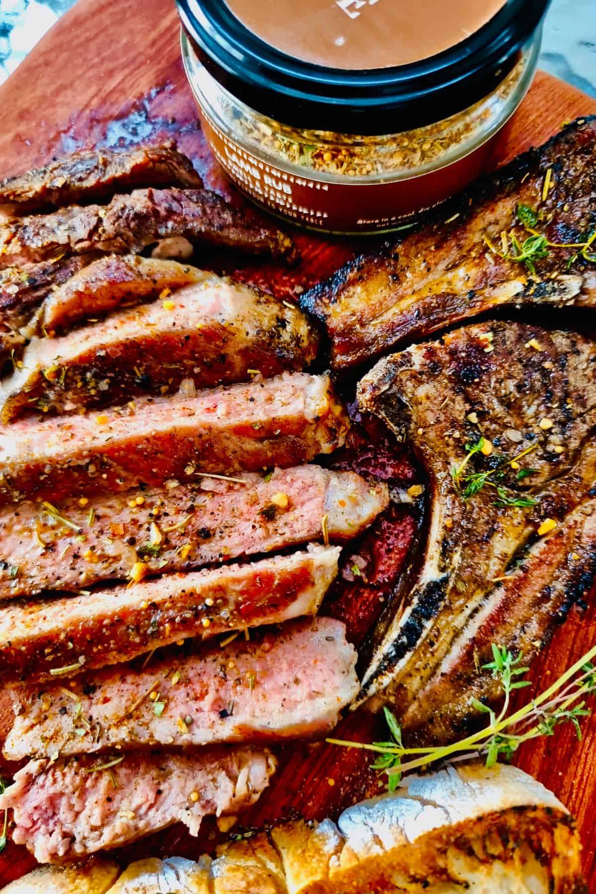 Cooked, herb- and spice-rubbed grilled lamb chops, sliced to show juicy pink center, served on a board.