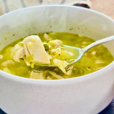 Chicken potato and pea soup in a bowl with a spoon lifting a scoop, with steam rising
