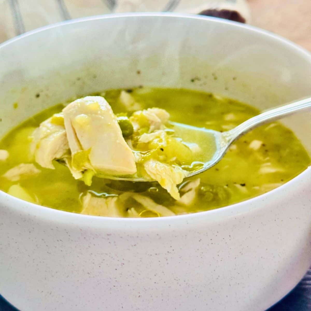 Chicken potato and pea soup in a bowl with a spoon lifting a scoop, with steam rising