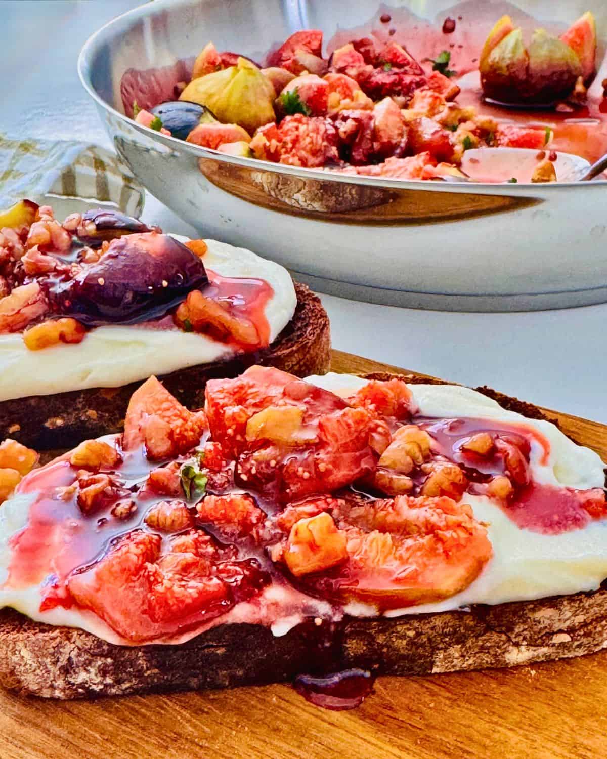 roasted figs in a balsamic glaze over mascarpone cheese and toast on a board. Pan in the background.
