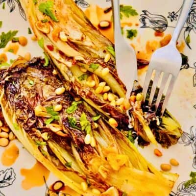grilled radicchio with pine nuts on a plate cut into with a knife and fork
