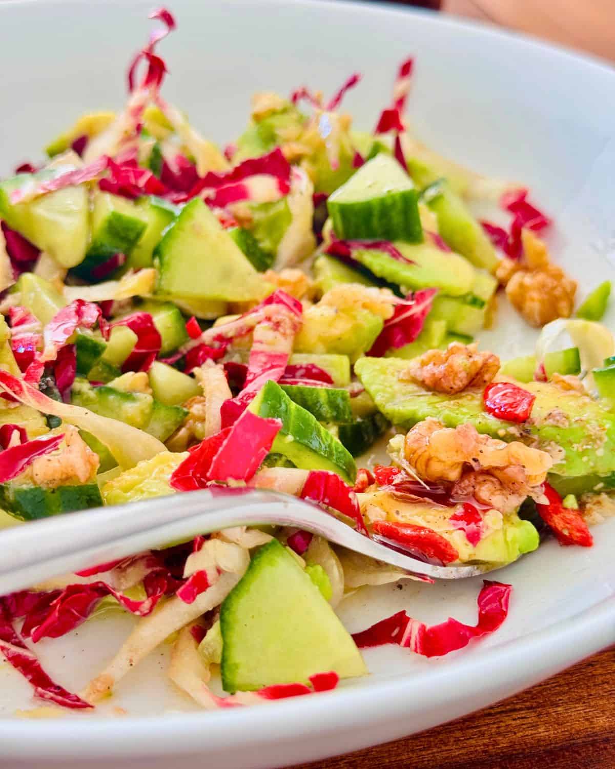 radicchio cucumber avocado and walnuts on a white plate with a fork.