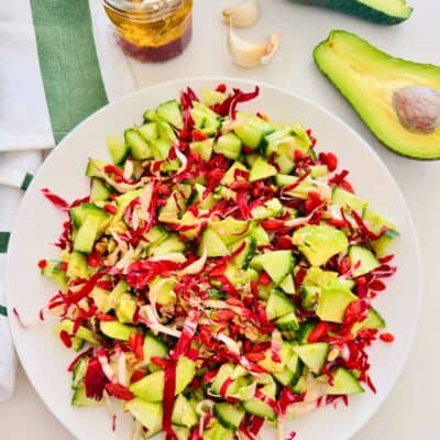 radicchio cucumber and avocado chopped salad on a white plate. Halved avocado, garlic and a mason jar with a vinaigrette next to it.