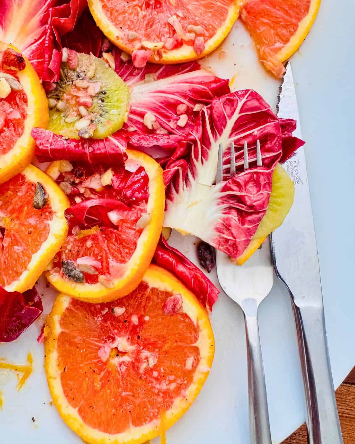 radicchio leaves on a white serving plate with orange and kiwi slices with a knife and fork.
