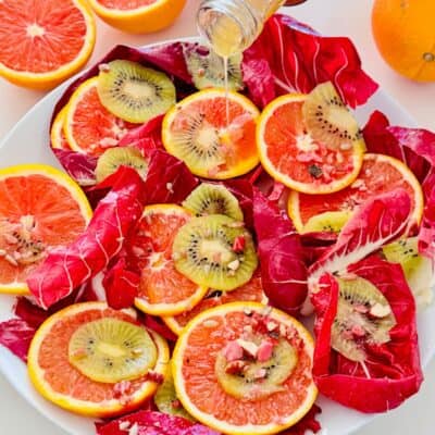 radicchio leaves on a white serving plate with orange slices, kiwi and a red wine vinaigrette poured over.