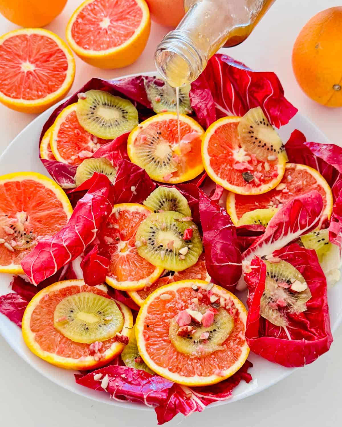 radicchio leaves on a white serving plate with orange slices, kiwi and a red wine vinaigrette poured over.