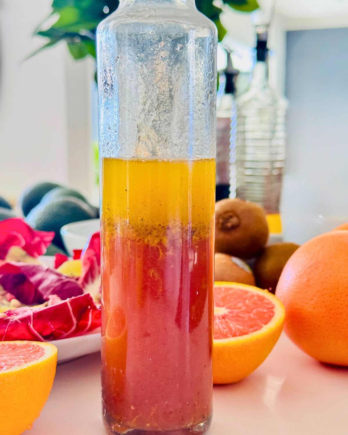 a bottle filled with homemade vinaigrette. Radicchio and oranges on the table .