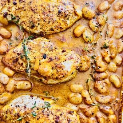 oven baked chicken and beans with sauce and thyme on a sheet pan.