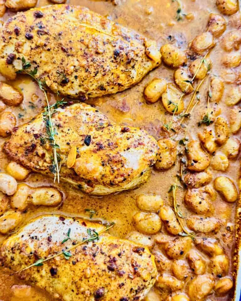 oven baked chicken and beans with sauce and thyme on a sheet pan.