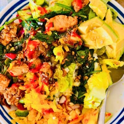 chicken and rice served in a bowl with pickles, hot sauce and avocado