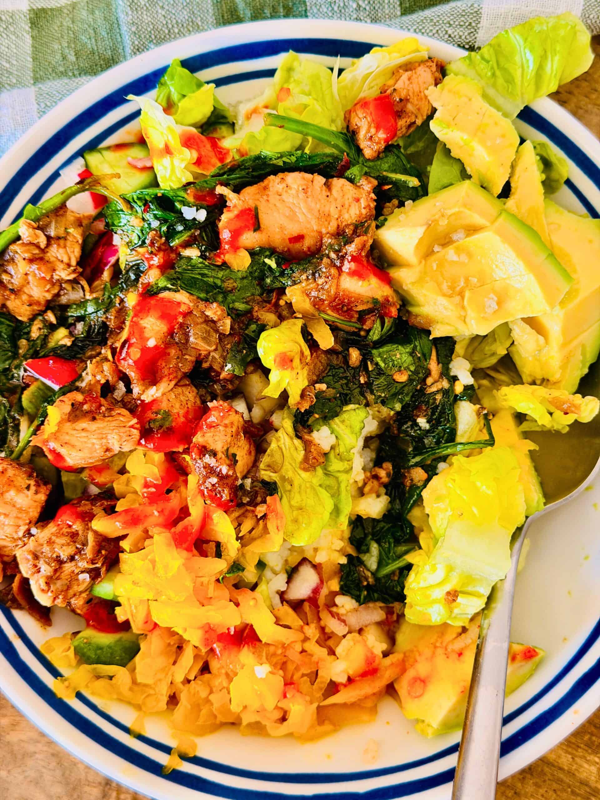 chicken and rice served in a bowl with pickles, hot sauce and avocado