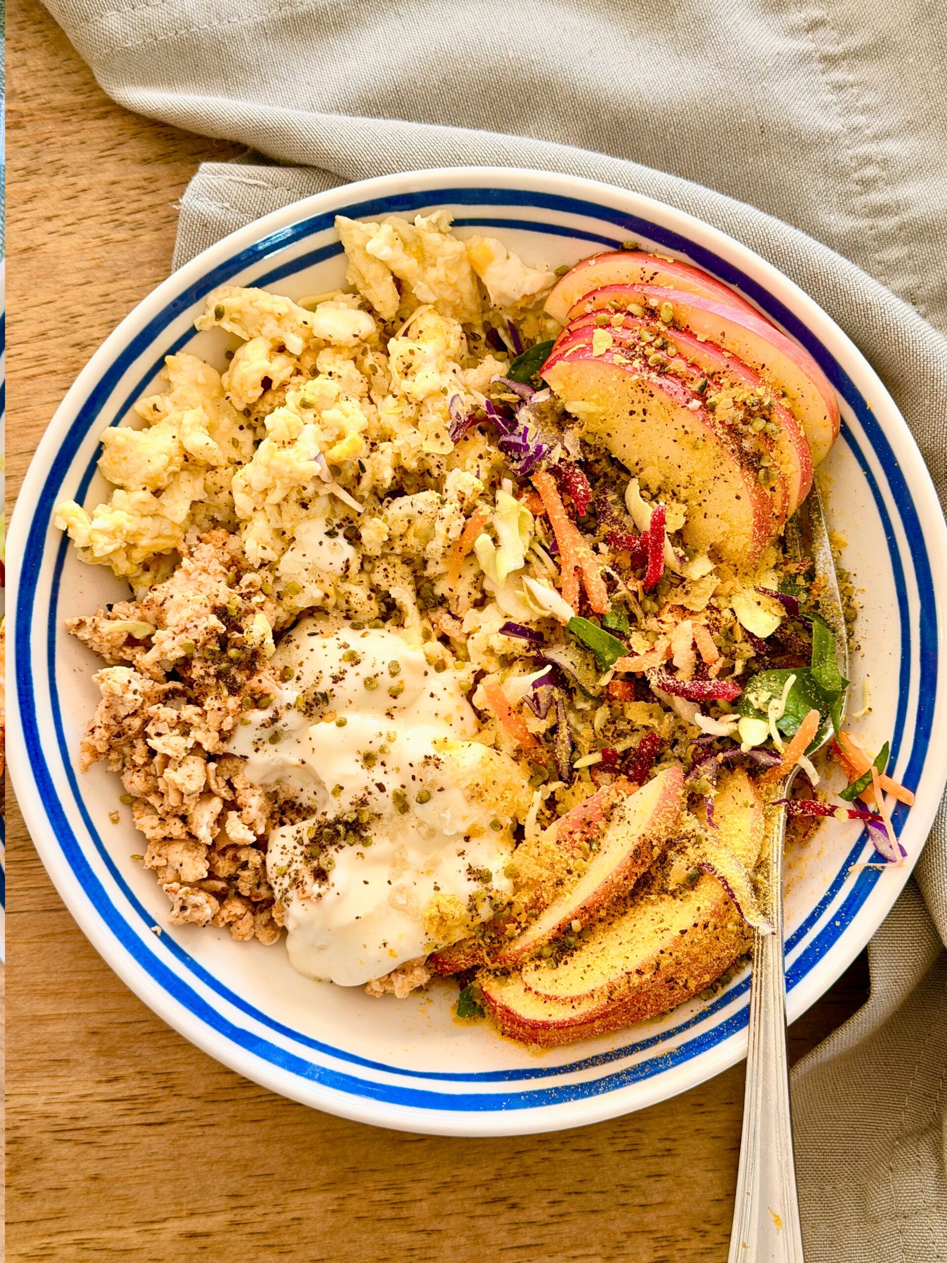 High-protein apple lunch bowl with scrambled eggs, ground chicken, rainbow slaw, sliced apple, yogurt and hemp seeds