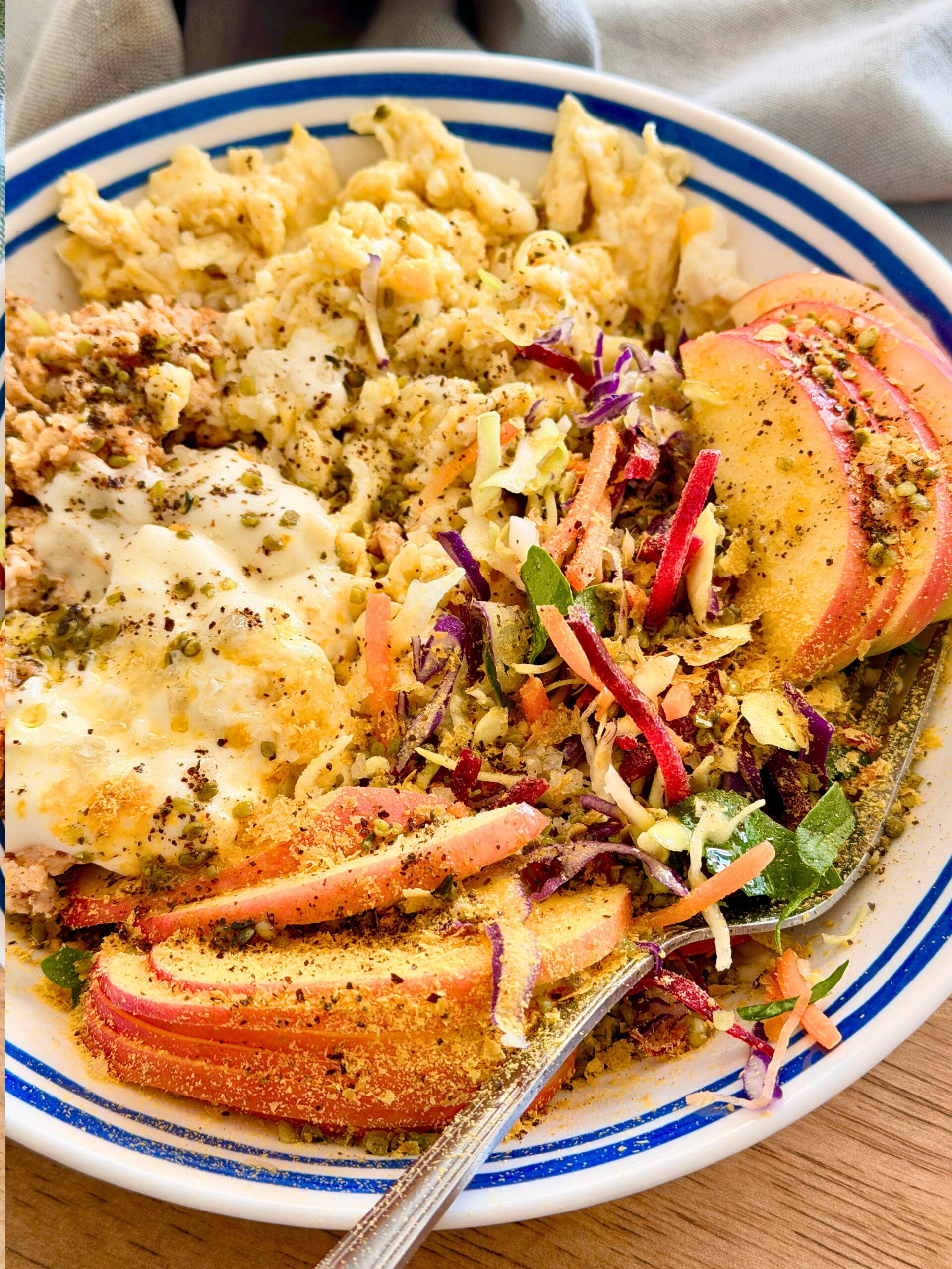 High-protein lunch bowl with scrambled eggs, ground chicken, rainbow slaw, sliced apple, yogurt and hemp seeds